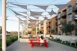 An airy canopy of tethered triangle shapes over deep sunset red picnic tables offers additional breaks from the sun without blocking views.