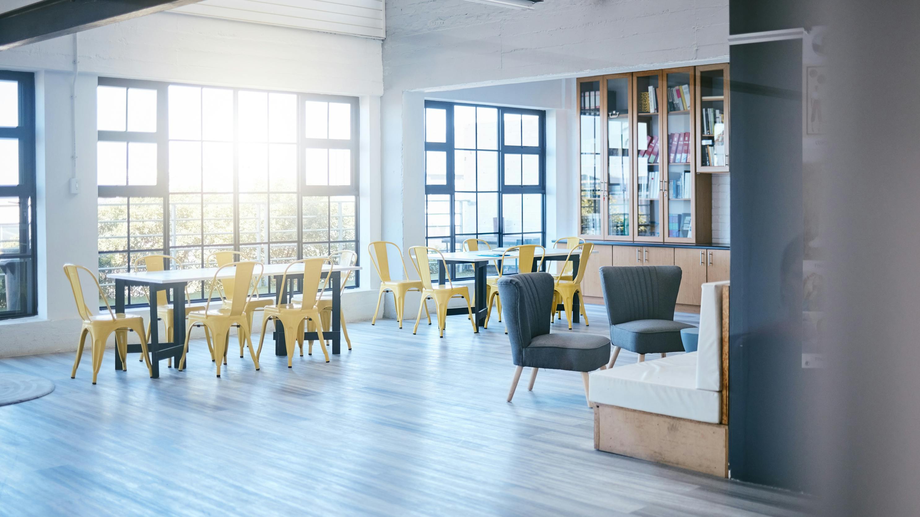 College study lounge with multiple seating arrangements, bookshelves, and large windows for daylight