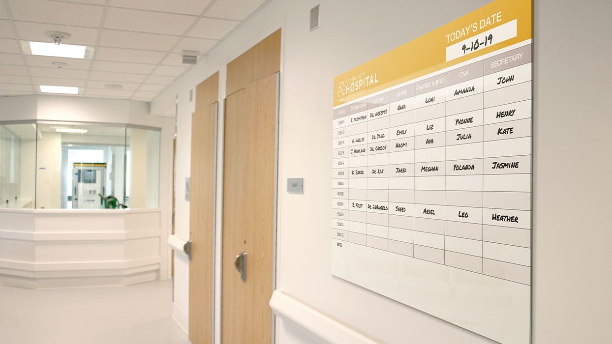 Ghent's low-profile Minimalist Graphic Glassboard installed in a hospital hallway. The glassboard displays names of hospital staff assigned to patient rooms.