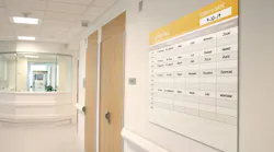 Ghent's low-profile Minimalist Graphic Glassboard installed in a hospital hallway. The glassboard displays names of hospital staff assigned to patient rooms.