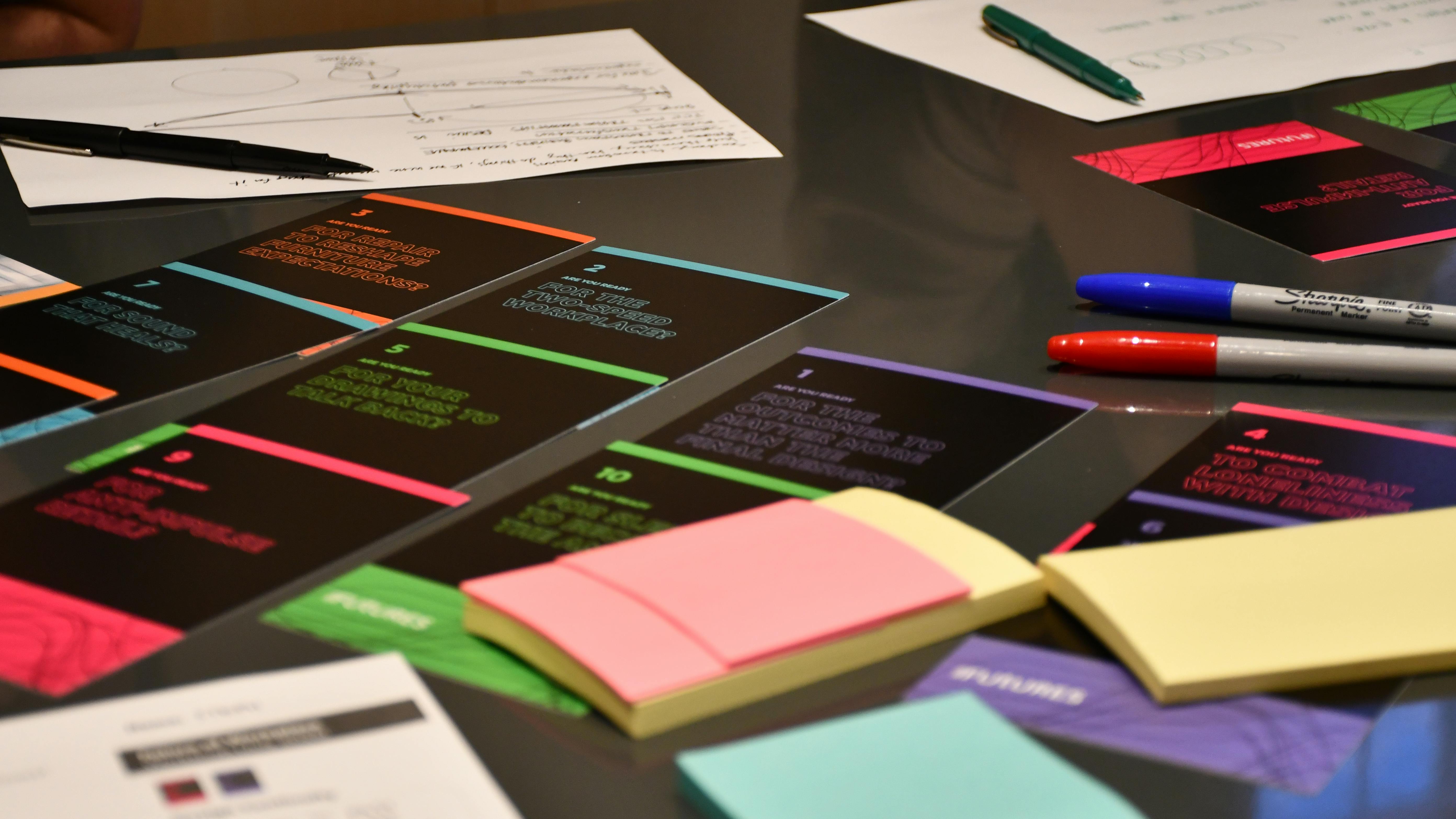 Assortment of notecards, Post-It notes, and markers spread out on a dark table.