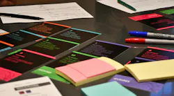 Assortment of notecards, Post-It notes, and markers spread out on a dark table.