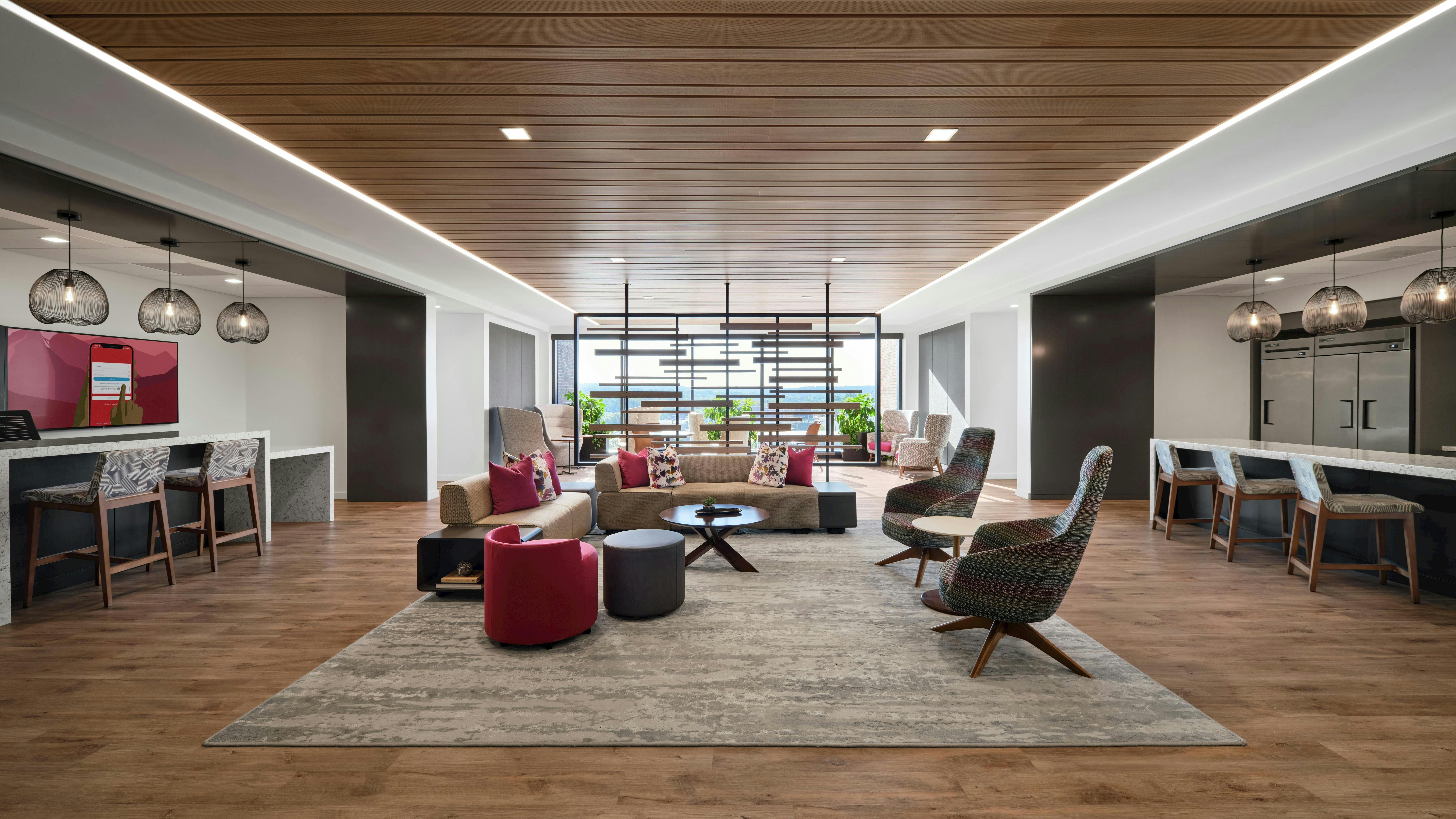 A large social space with layered lighting, daylight access, and multiple seating arrangements from a central lounge setup to counters with task chairs and individual soft seating.