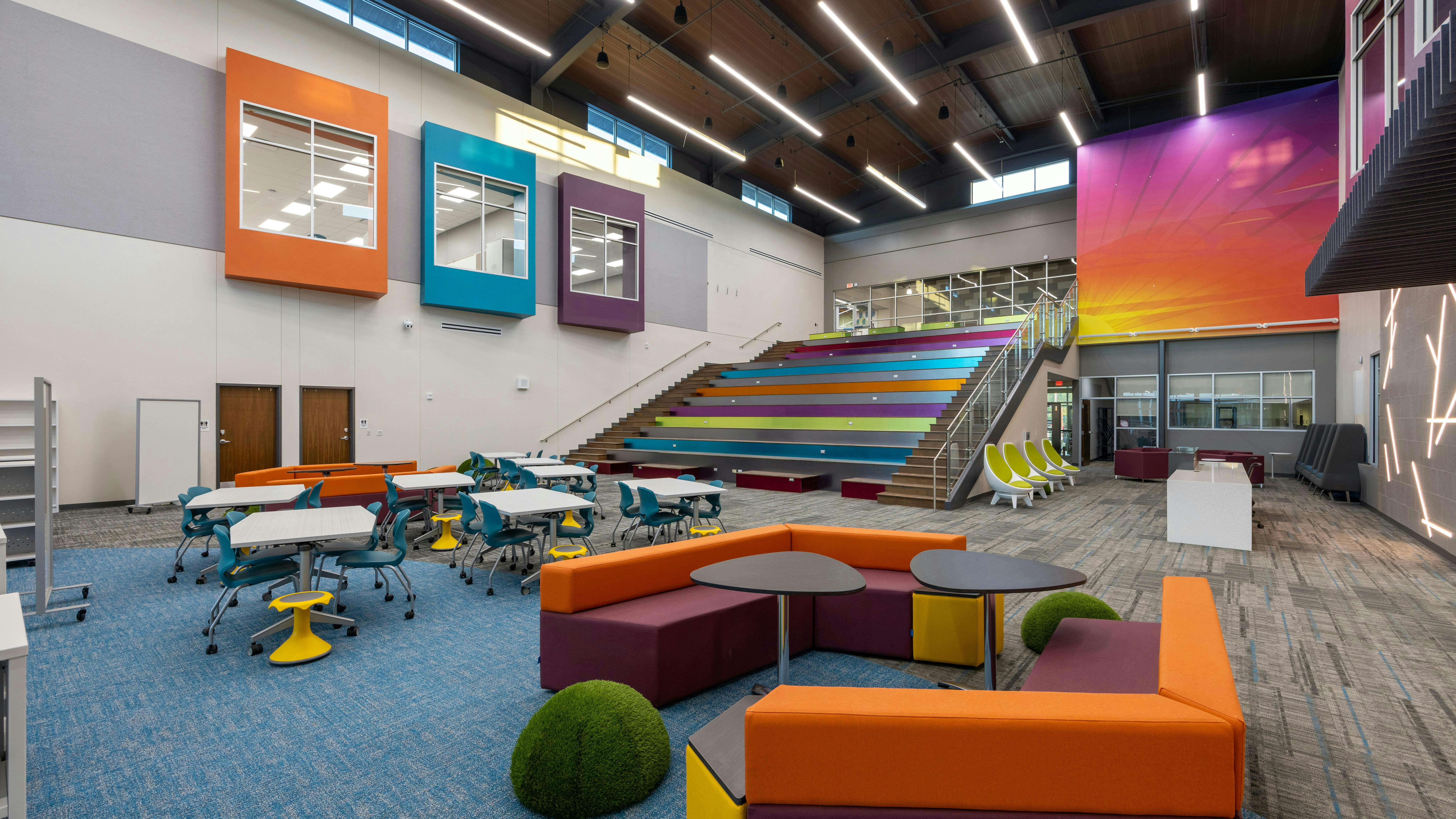 Colorful elementary school library with stadium-style seating on stairs, and tables grouped with moveable chairs