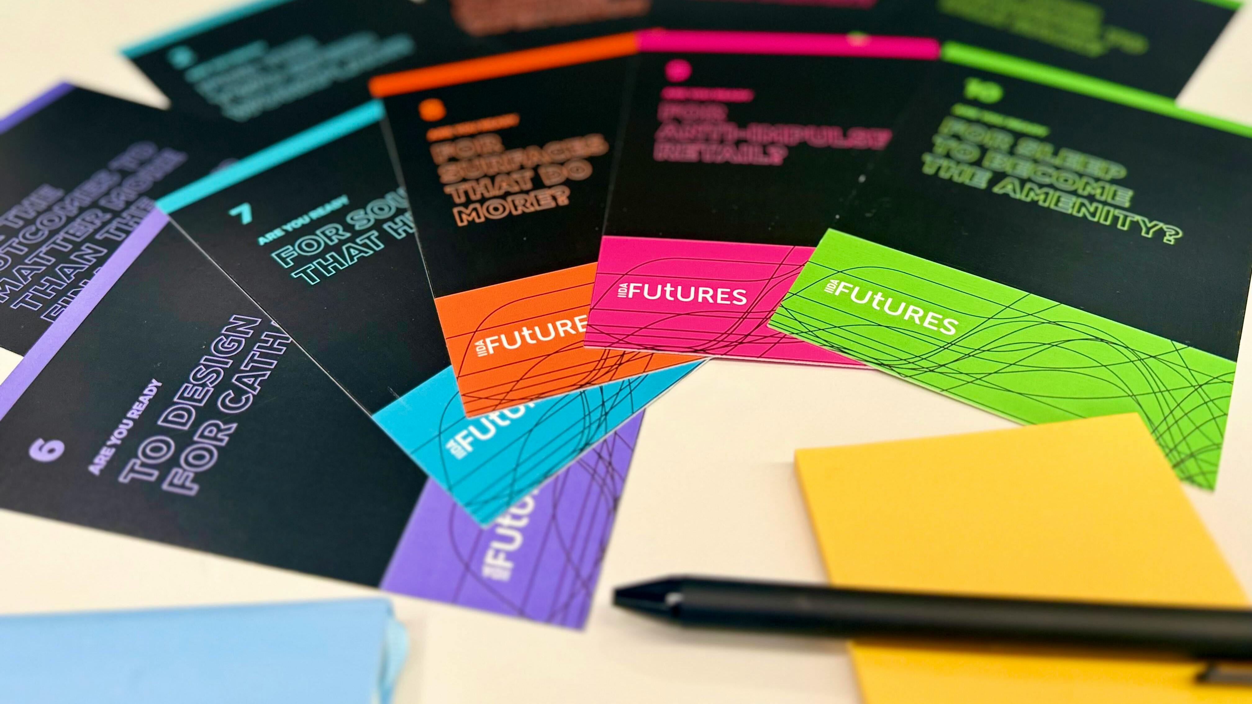 Various array of cards with provocative questions about the future of design spread across table with pens and sticky notes.