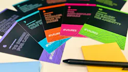 Various array of cards with provocative questions about the future of design spread across table with pens and sticky notes.