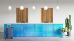 A reception desk with 3form's Pearlescent in midnight installed on the front. Luggage and faux cacti accent the desk.