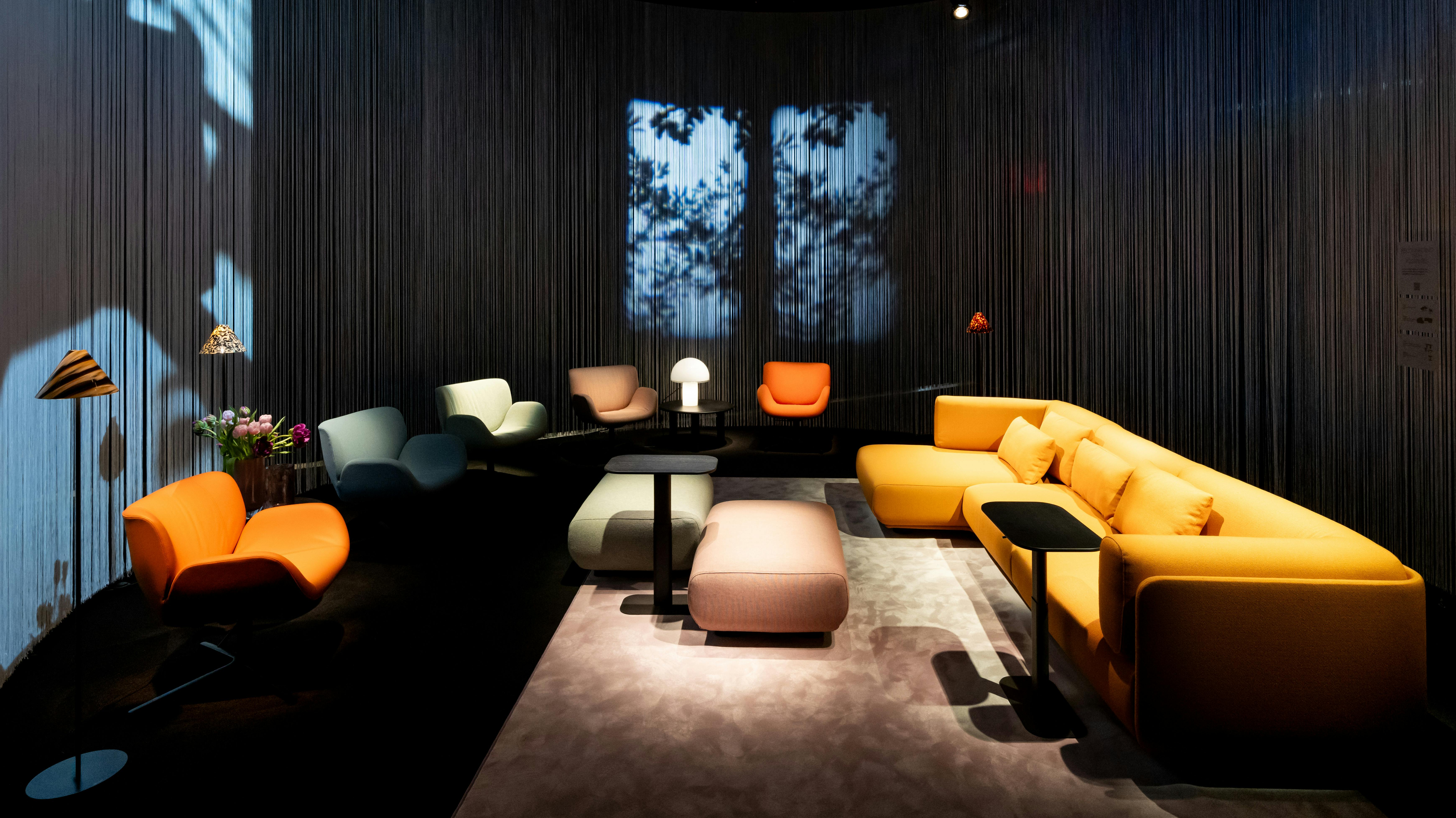 A variety of soft, colorful lounge seating in dramatically lit space with shadow of trees in background.
