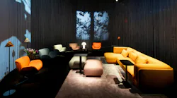 A variety of soft, colorful lounge seating in dramatically lit space with shadow of trees in background.