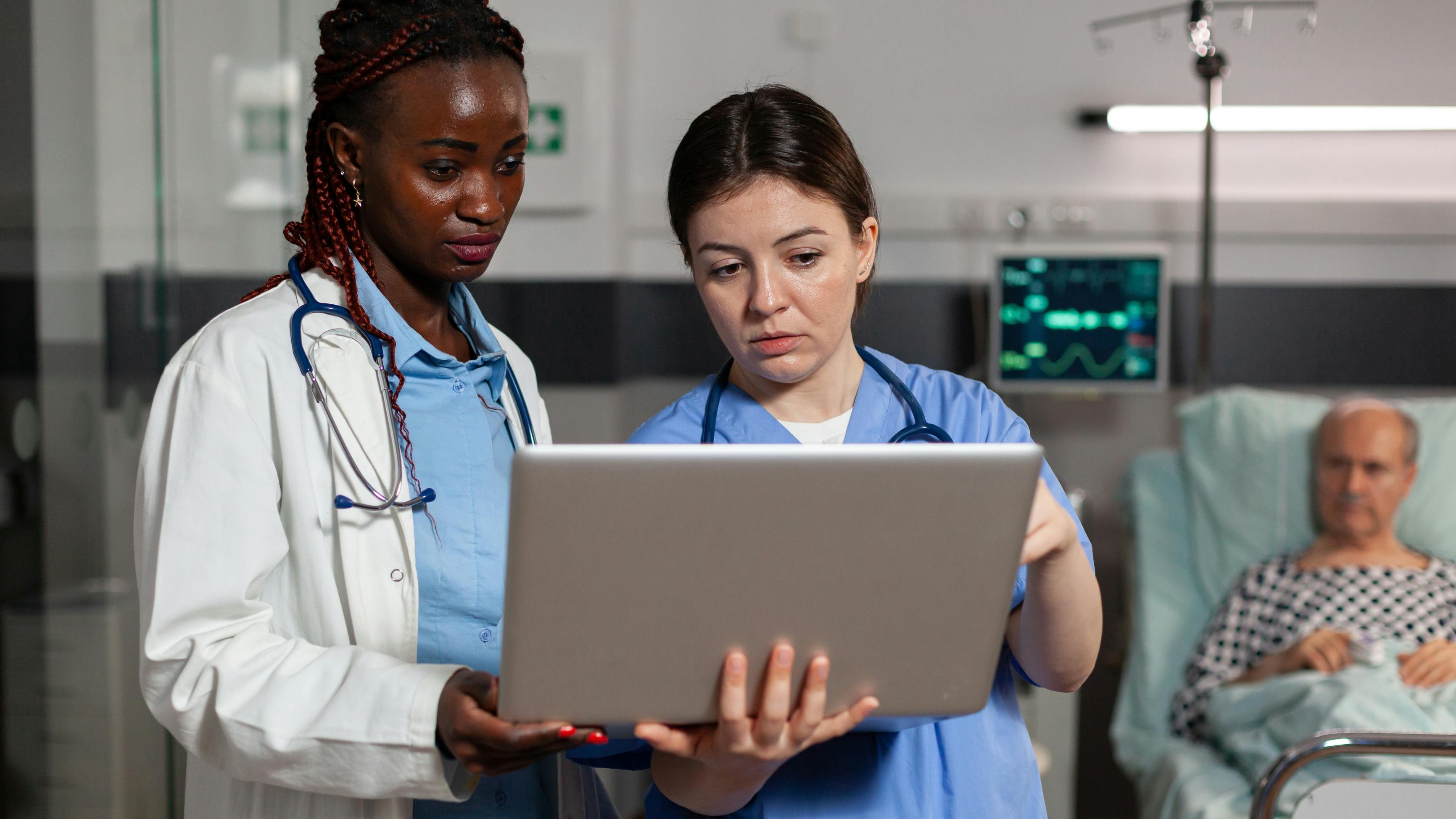 Black female doctor and white female nurse discussing care plan, with senior white male patient in the background