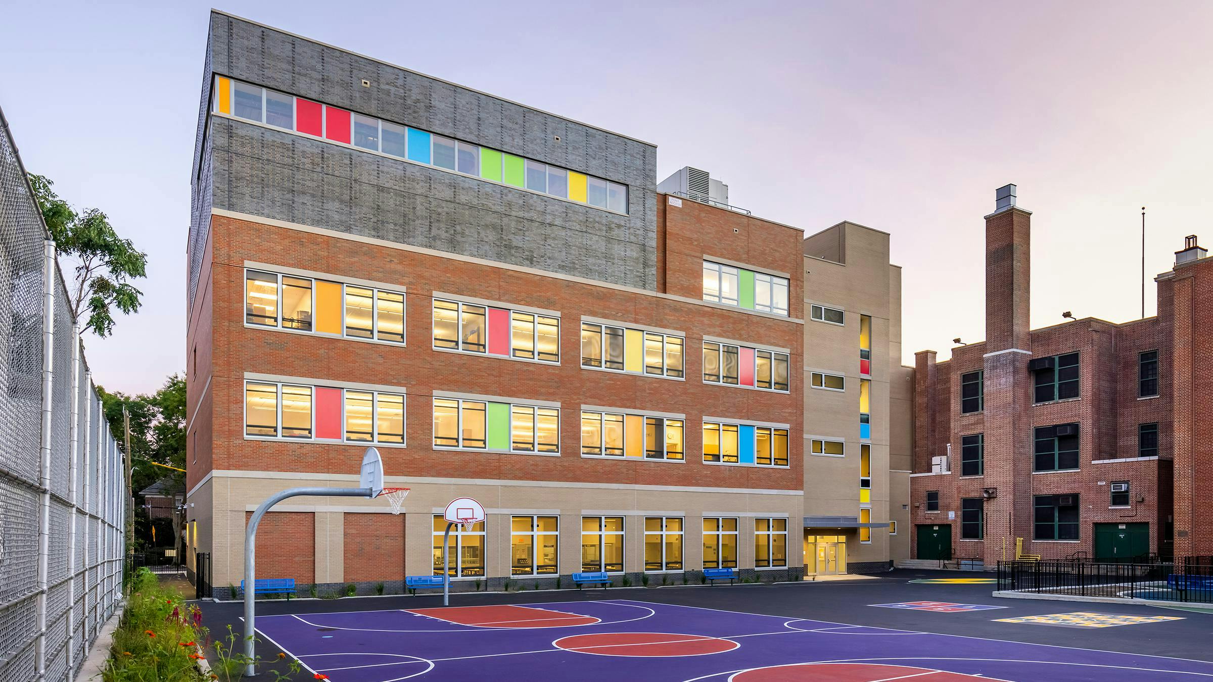 Exterior view of public school with colorful window and facade accents, backed up to a red and purple sports court area