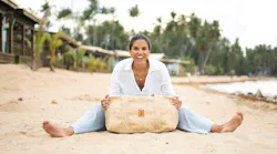 Joy Reyes, founder and CEO of New Hope Girls, sits on the beach with a bag made from Nassimi fabric.
