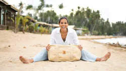 Joy Reyes, founder and CEO of New Hope Girls, sits on the beach with a bag made from Nassimi fabric.
