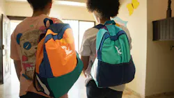 Two students carry backpacks made by New Hope Girls through a school hallway. Women use donated fabrics to create backpacks for kids in the Dominican Republic.