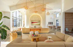 At Alma Apartments, a comfortable lounge opens to individual seating along expansive windows, café-style tables and banquettes opposite, and another flexible gathering zone to the right of the lounge.