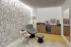 Lactation room features comfortable upholstered lounge and ottoman, cabinetry with small sink and refrigerator, and custom line drawing used as a wall graphic