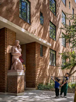 Two young Black children stand in front of the restored Mother and Child with Dog sculpture, with a glimpse of newly painted passageway mural showing