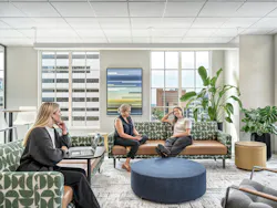 Three female employees collaborate in a casual seating area with green and white patterned sofas, neutral accessories, and patterned carpeting that visually references variation found in stone