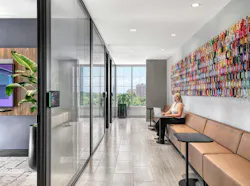Cushioned bench seating along an interior wall accommodates multiple laptop-sized tables for free desking, across from a glass-walled conference room