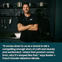Massimo Buster Minale, Buster + Punch founder, stands in front of a kitchen display with dark green walls and cabinetry and stainless steel cookware and appliances