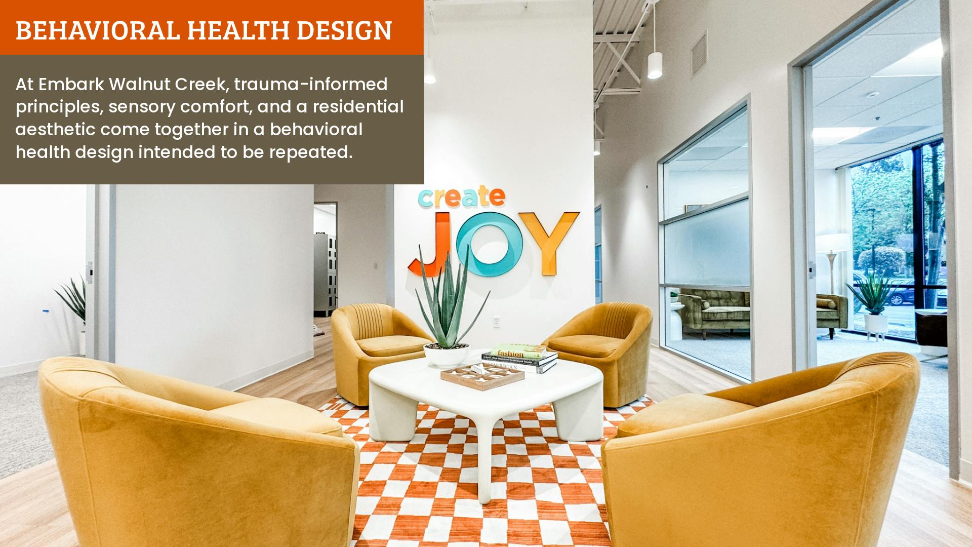 Open lounge area with Create Joy wall sign, golden yellow barrel chairs, and and orange and white checkered area rug