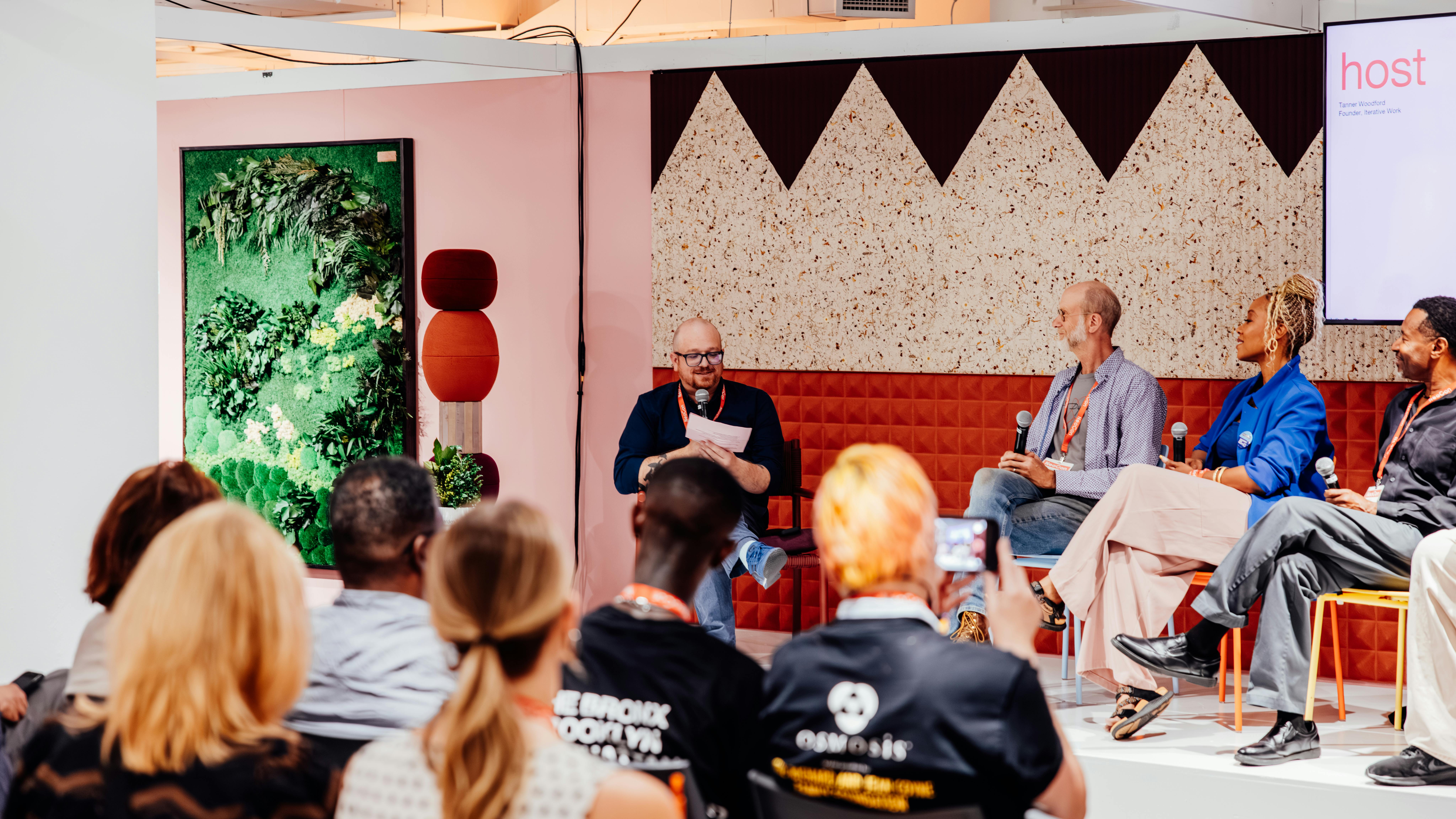 Tanner Woodford, founder of Iterative Work, moderates a panel discussion of four guests on stage at NeoCon 2026, in Chicago. Audience members sit in chairs and listen to the discussion. The 2027 NeoCon Call for Programming opened in October 2026.