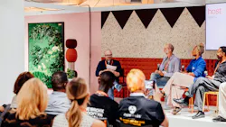 Tanner Woodford, founder of Iterative Work, moderates a panel discussion of four guests on stage at NeoCon 2026, in Chicago. Audience members sit in chairs and listen to the discussion. The 2027 NeoCon Call for Programming opened in October 2026.